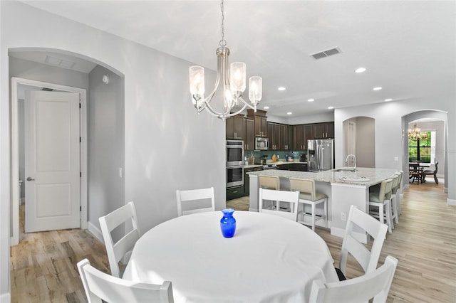 dining space with light wood-style floors, visible vents, arched walkways, and a notable chandelier