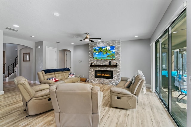 living room with ceiling fan, a stone fireplace, light hardwood / wood-style flooring, and a textured ceiling