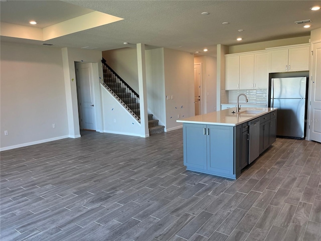 kitchen with stainless steel fridge, dark hardwood / wood-style flooring, sink, white cabinetry, and a kitchen island with sink