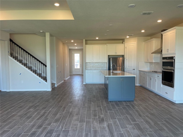 kitchen featuring appliances with stainless steel finishes, dark wood-type flooring, an island with sink, and white cabinets