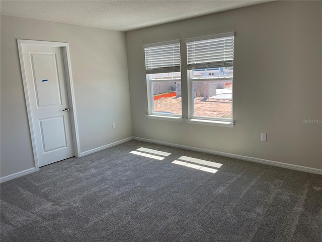 spare room featuring dark colored carpet and a textured ceiling