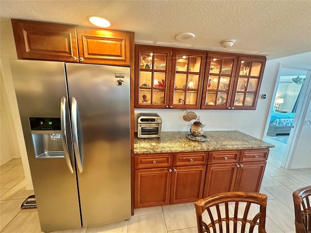 kitchen with a textured ceiling, light tile patterned floors, light stone counters, and stainless steel refrigerator with ice dispenser