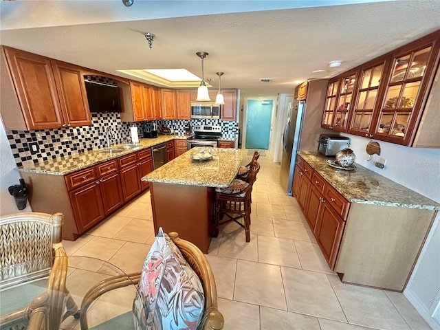 kitchen featuring stainless steel appliances, light stone countertops, pendant lighting, a center island, and a breakfast bar