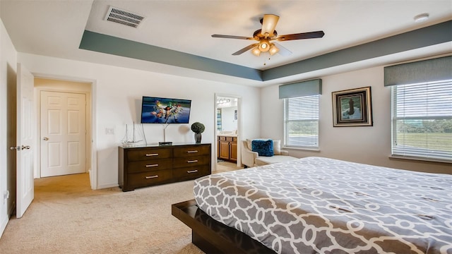 carpeted bedroom featuring ceiling fan, ensuite bath, and a tray ceiling