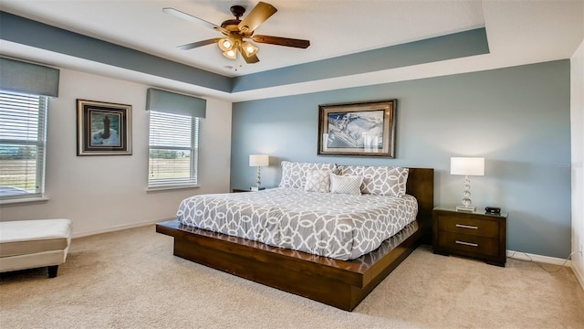 bedroom with ceiling fan, a raised ceiling, and light colored carpet