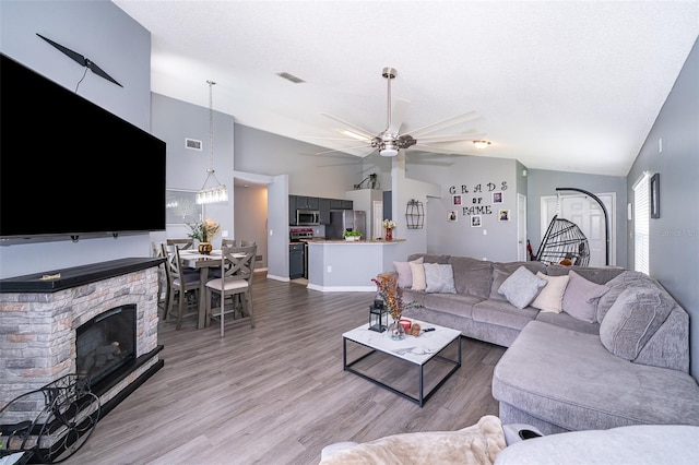 living room with ceiling fan, a fireplace, high vaulted ceiling, and light hardwood / wood-style flooring