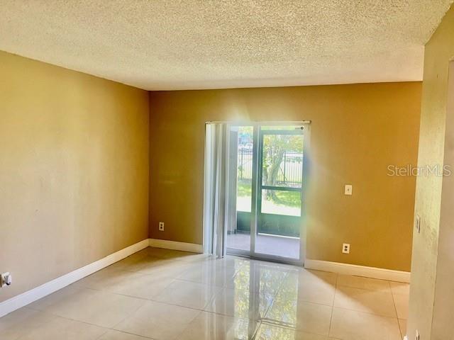 spare room with light tile patterned flooring, a textured ceiling, and baseboards