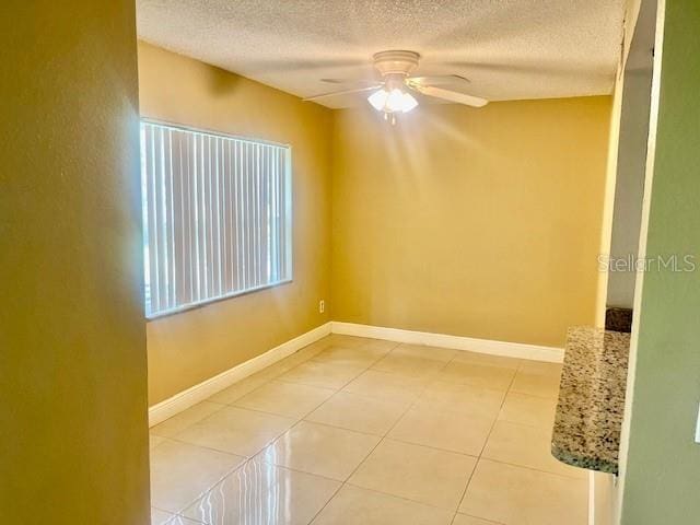 empty room featuring ceiling fan, a textured ceiling, light tile patterned flooring, and baseboards