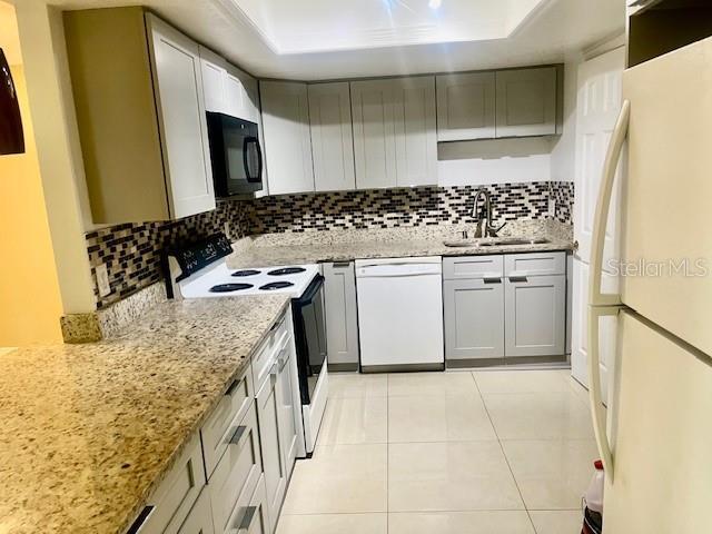 kitchen with white appliances, tasteful backsplash, a raised ceiling, and a sink