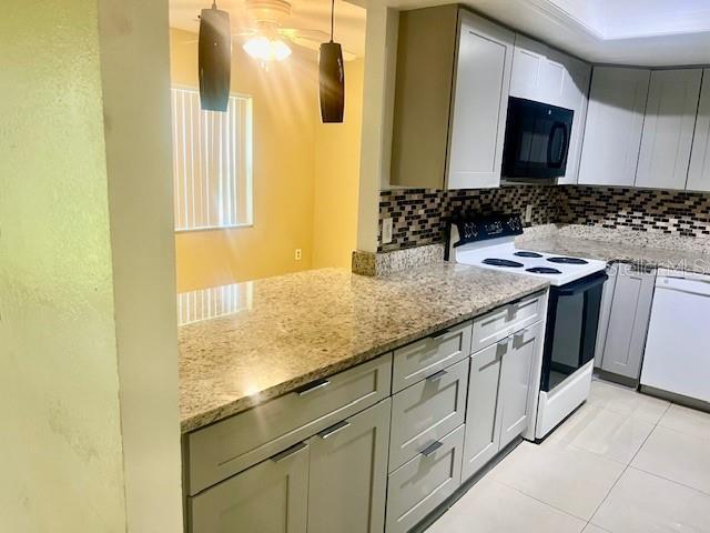 kitchen featuring white appliances, light tile patterned floors, light stone counters, and backsplash