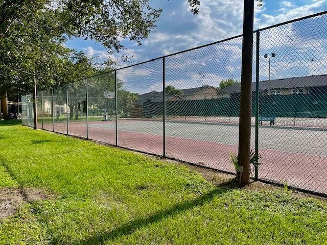 view of tennis court featuring community basketball court, a lawn, and fence