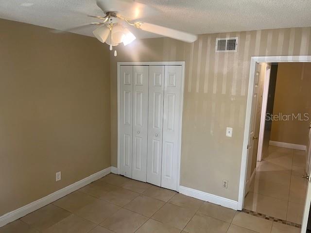 unfurnished bedroom with a textured ceiling, visible vents, baseboards, a closet, and wallpapered walls