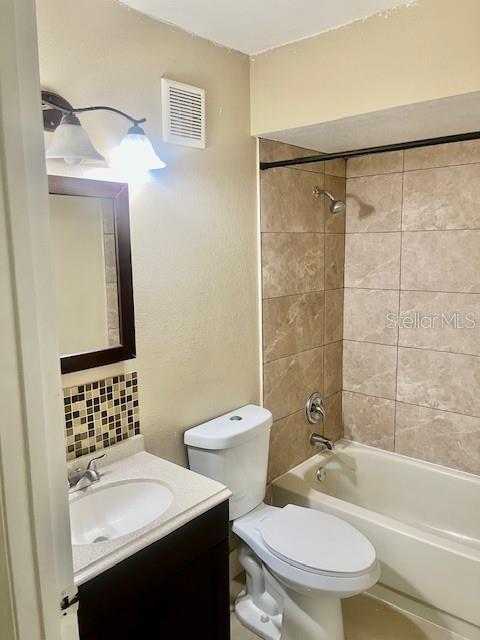 full bath featuring tasteful backsplash, visible vents, toilet, vanity, and washtub / shower combination