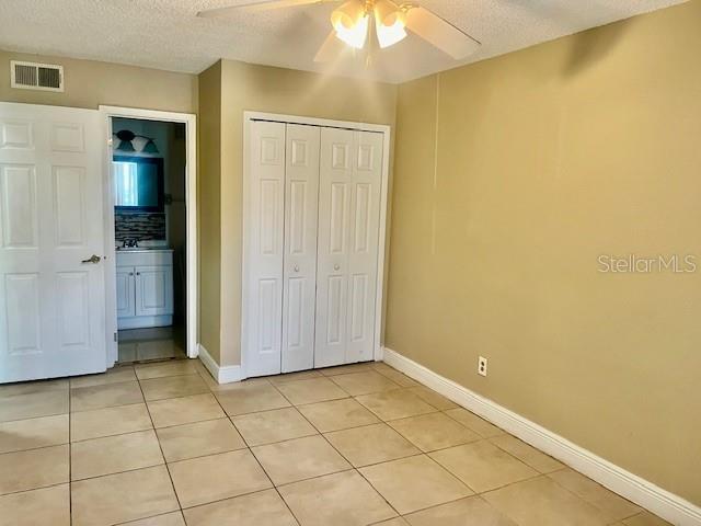 unfurnished bedroom featuring light tile patterned floors, a closet, visible vents, a textured ceiling, and baseboards