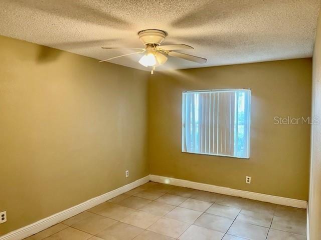 spare room with ceiling fan, light tile patterned floors, a textured ceiling, and baseboards