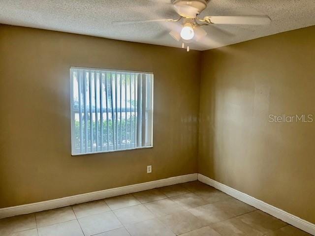 unfurnished room with a textured ceiling, light tile patterned floors, a ceiling fan, and baseboards