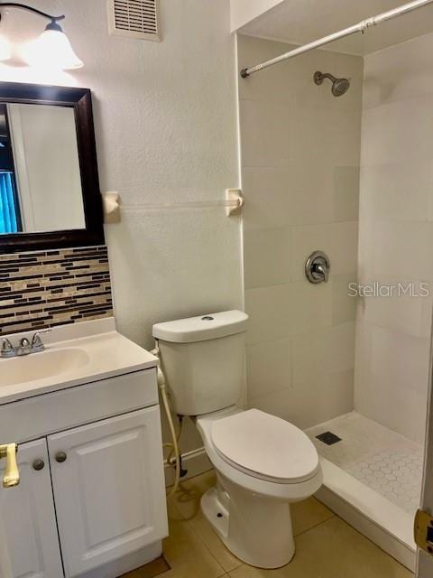 full bathroom featuring toilet, a tile shower, visible vents, and decorative backsplash