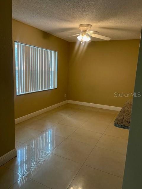 spare room with light tile patterned floors, a textured ceiling, baseboards, and a ceiling fan