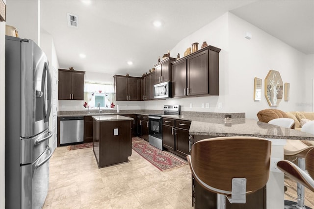 kitchen featuring stainless steel appliances, light stone counters, light tile patterned floors, a kitchen island, and a breakfast bar