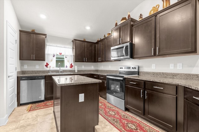 kitchen featuring appliances with stainless steel finishes, light stone countertops, light tile patterned floors, sink, and a center island