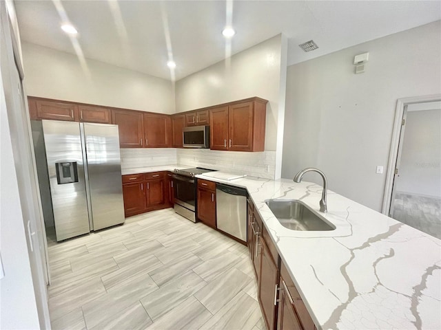 kitchen with decorative backsplash, a towering ceiling, light stone counters, sink, and stainless steel appliances