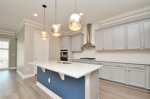 kitchen with gray cabinetry, decorative light fixtures, stainless steel appliances, a kitchen island with sink, and wall chimney range hood