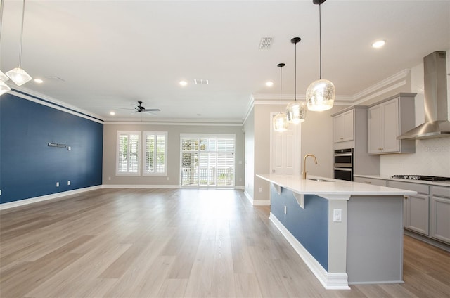 kitchen with wall chimney range hood, gray cabinets, a kitchen bar, light hardwood / wood-style floors, and sink