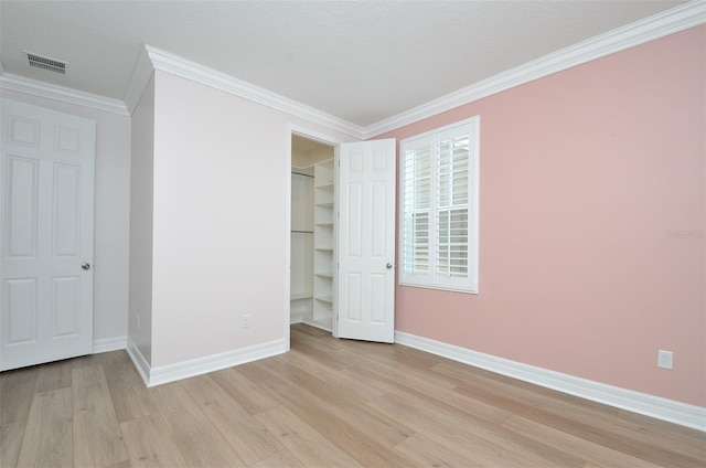 unfurnished bedroom with ornamental molding, a spacious closet, a closet, and light wood-type flooring