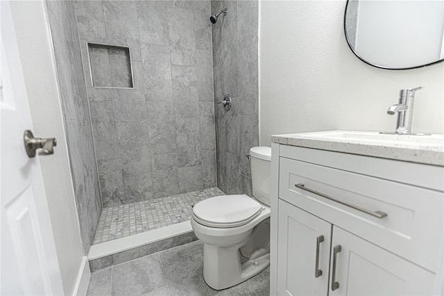 bathroom featuring tile patterned flooring, vanity, toilet, and a tile shower