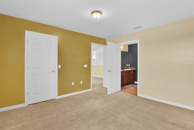 unfurnished bedroom featuring light carpet and ensuite bath