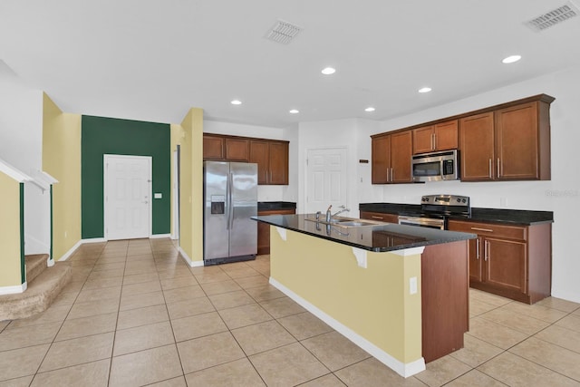 kitchen featuring light tile patterned floors, an island with sink, dark stone counters, sink, and stainless steel appliances