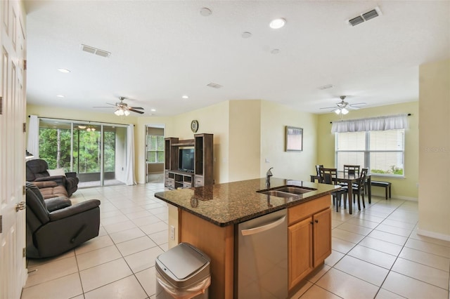 kitchen featuring an island with sink, stainless steel dishwasher, sink, ceiling fan, and dark stone counters