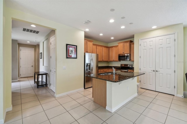 kitchen with dark stone countertops, stainless steel appliances, an island with sink, sink, and a breakfast bar