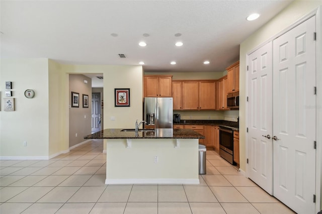 kitchen featuring dark stone countertops, appliances with stainless steel finishes, sink, an island with sink, and a breakfast bar