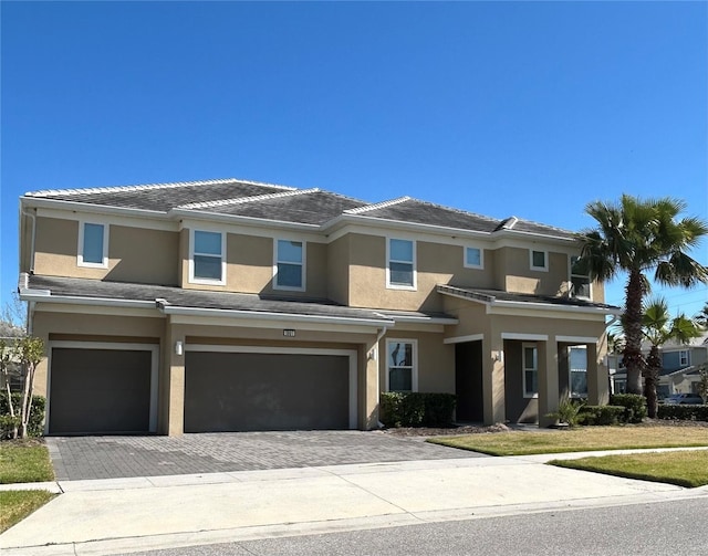 view of front of house featuring a tiled roof, stucco siding, an attached garage, and decorative driveway