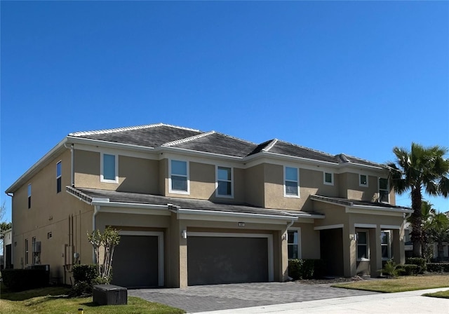 view of front of home featuring decorative driveway, a tile roof, an attached garage, and stucco siding