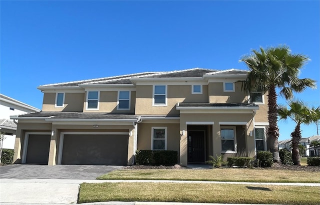 prairie-style home with a tiled roof, a front yard, stucco siding, decorative driveway, and a garage