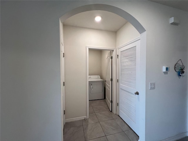 corridor featuring light tile patterned floors, washer / clothes dryer, arched walkways, and baseboards