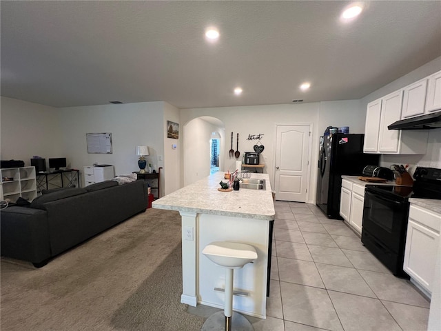 kitchen featuring arched walkways, black electric range, light countertops, white cabinets, and an island with sink