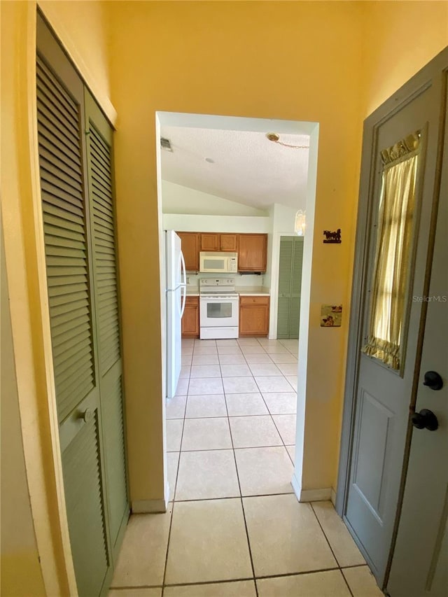 hallway featuring vaulted ceiling and light tile patterned flooring