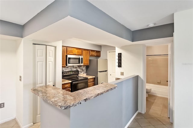 kitchen featuring appliances with stainless steel finishes, light tile patterned floors, kitchen peninsula, and tasteful backsplash