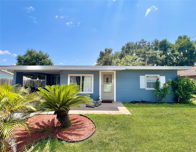ranch-style house featuring concrete block siding, fence, and a front lawn