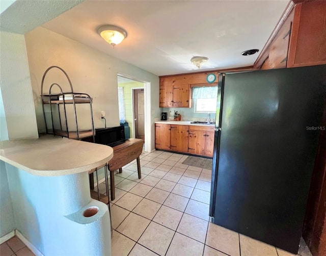 kitchen featuring sink, light tile patterned flooring, and black refrigerator