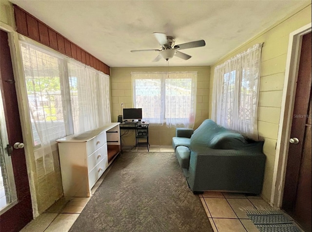 home office with ceiling fan, light tile patterned flooring, and wood walls