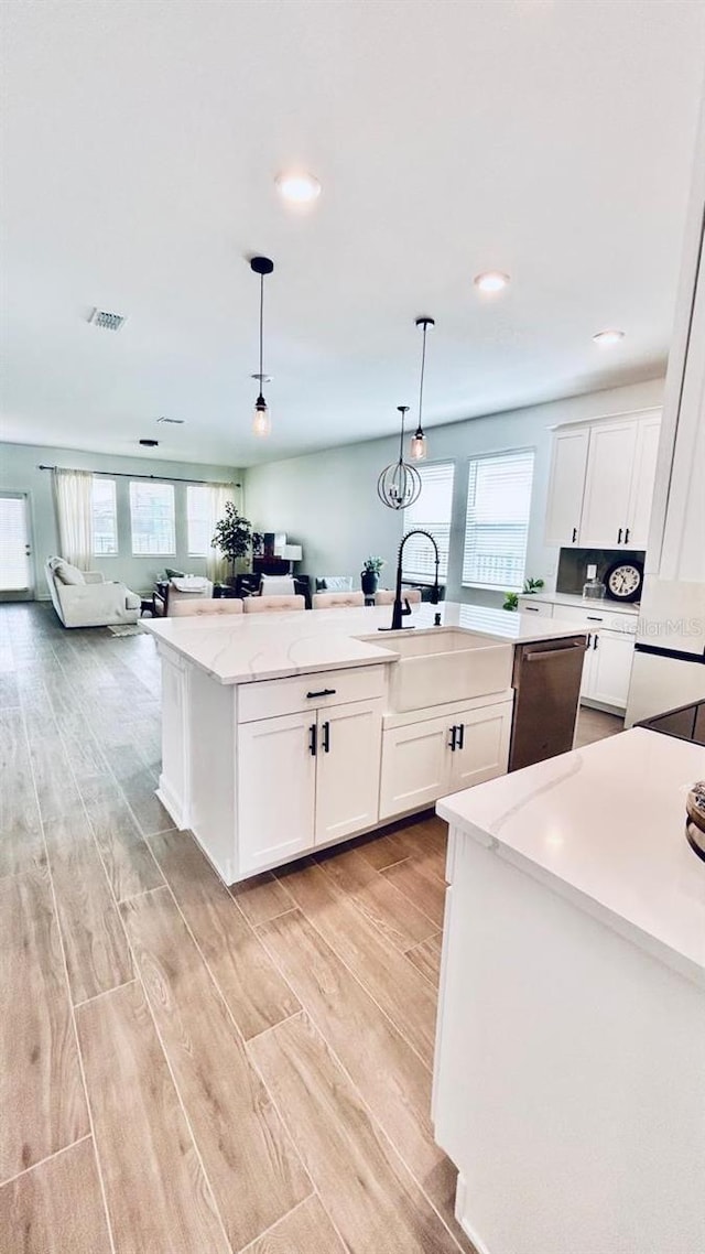 kitchen featuring light hardwood / wood-style flooring, stainless steel dishwasher, light stone countertops, decorative light fixtures, and a center island with sink