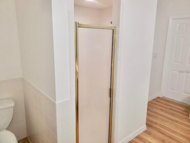 bathroom with toilet, a shower stall, tile walls, and wood finished floors