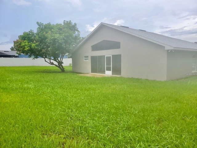 back of house with stucco siding, a lawn, and fence