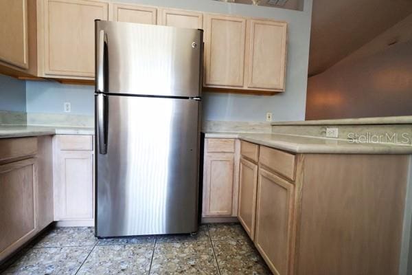 kitchen featuring stainless steel fridge, light tile patterned flooring, and light brown cabinetry