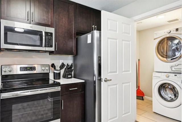 kitchen with stainless steel appliances, stacked washer and clothes dryer, light tile patterned floors, and dark brown cabinets