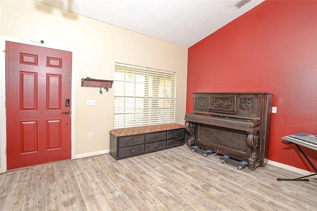 foyer entrance featuring a textured ceiling, light hardwood / wood-style flooring, and vaulted ceiling